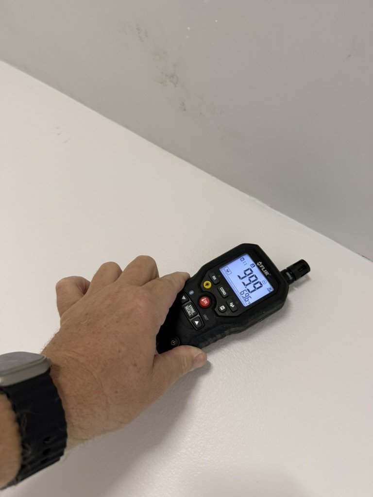 FLIR handheld moisture meter placed on a ceiling surface during the Lauderhill roof leak investigation, with dark marks visible on the adjoining surface.
