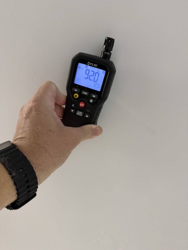 FLIR handheld moisture meter held against an apartment ceiling during the roof leak investigation.