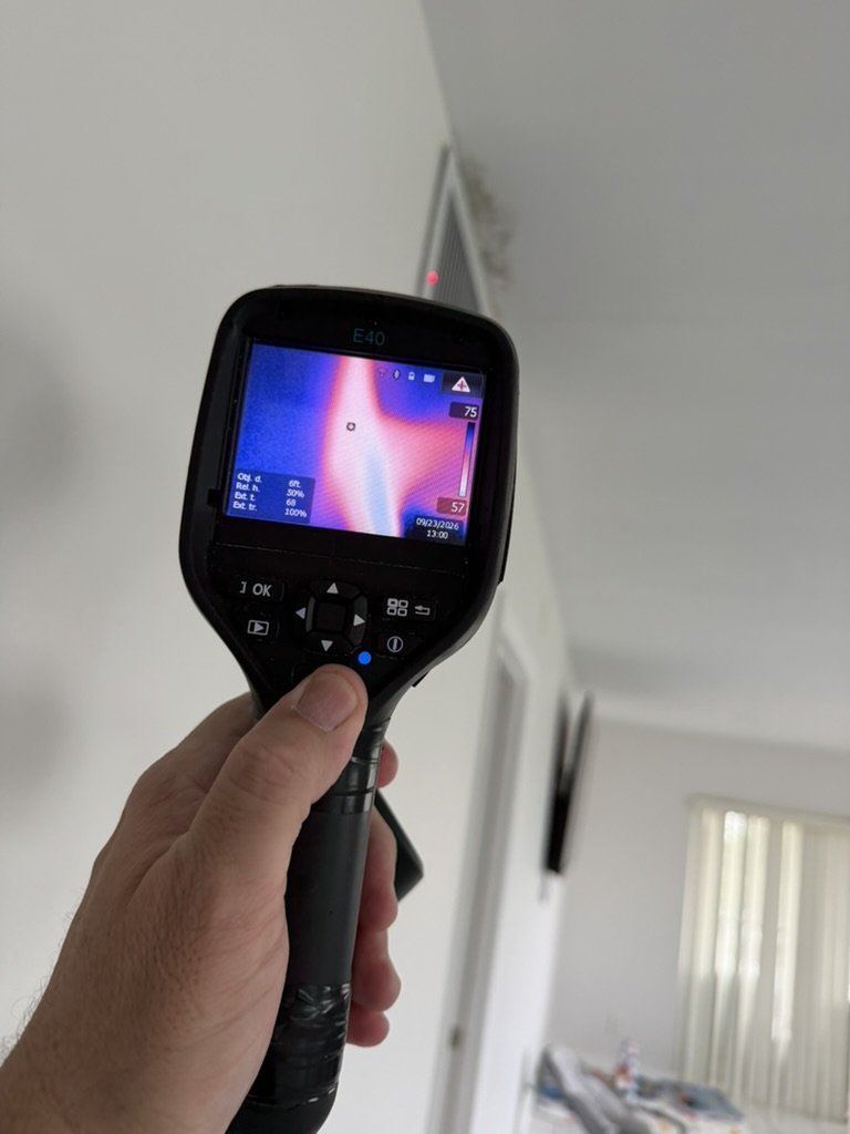 FLIR E40 thermal imaging camera scanning the TV and dining room ceiling beside the air conditioning grille, where water-related staining was observed.