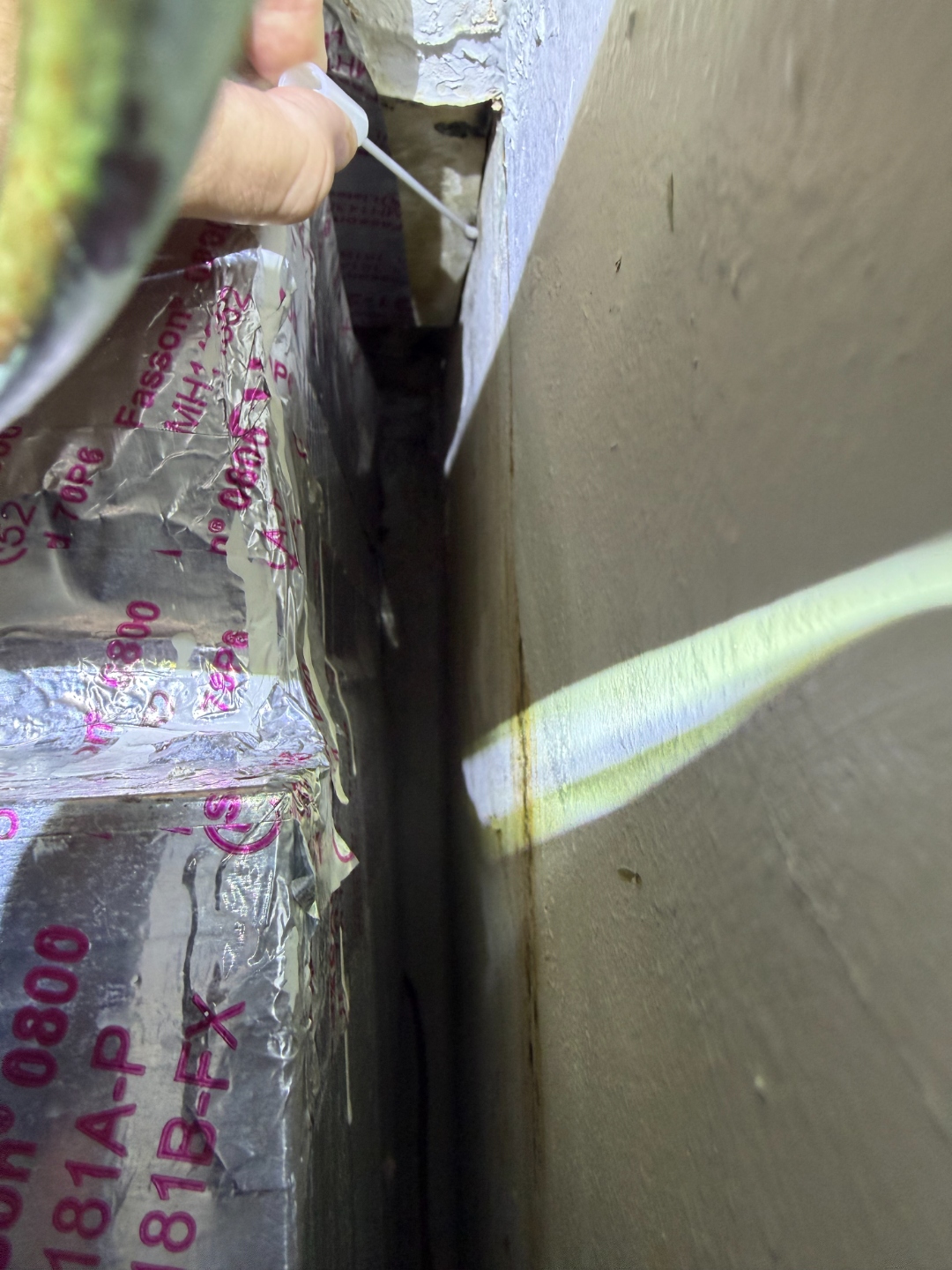 Close-up view of staining and deterioration in a narrow gap behind the air handler, accessed with a probe tool.