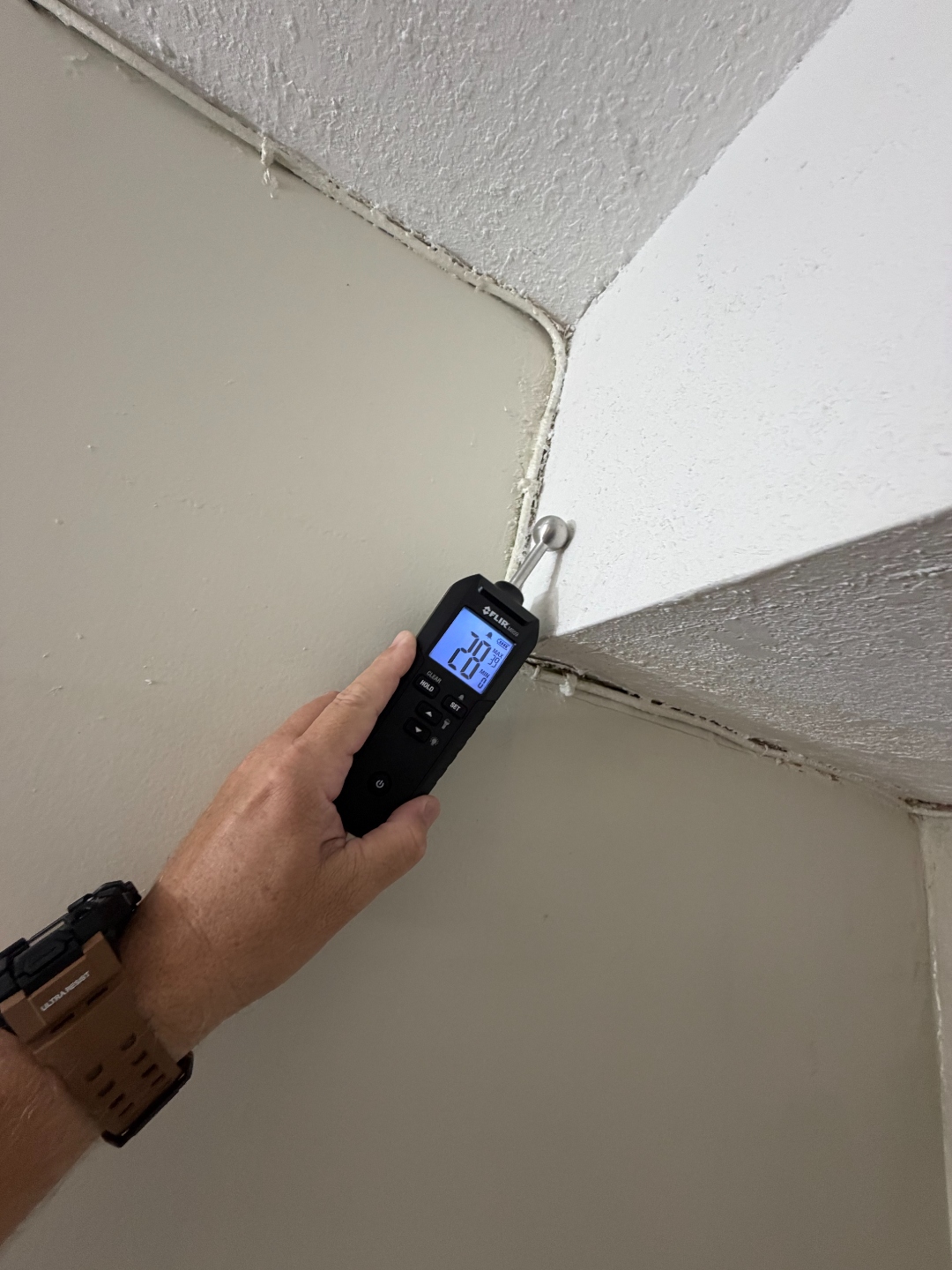 FLIR pin-type moisture meter taking a reading at a ceiling-to-wall corner near the AC closet.