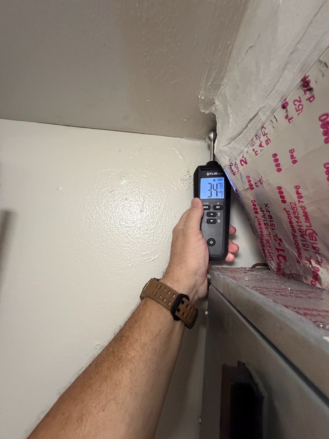 FLIR pin-type moisture meter reading taken at a ceiling-to-wall transition adjacent to insulated ductwork.