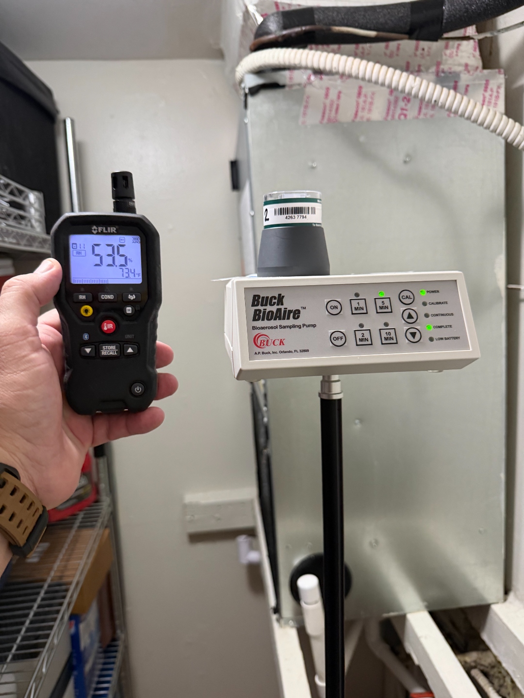 FLIR hygrometer displaying approximately 53.5% relative humidity and 73.4 degrees Fahrenheit, with a Buck BioAire air sampling pump staged nearby.